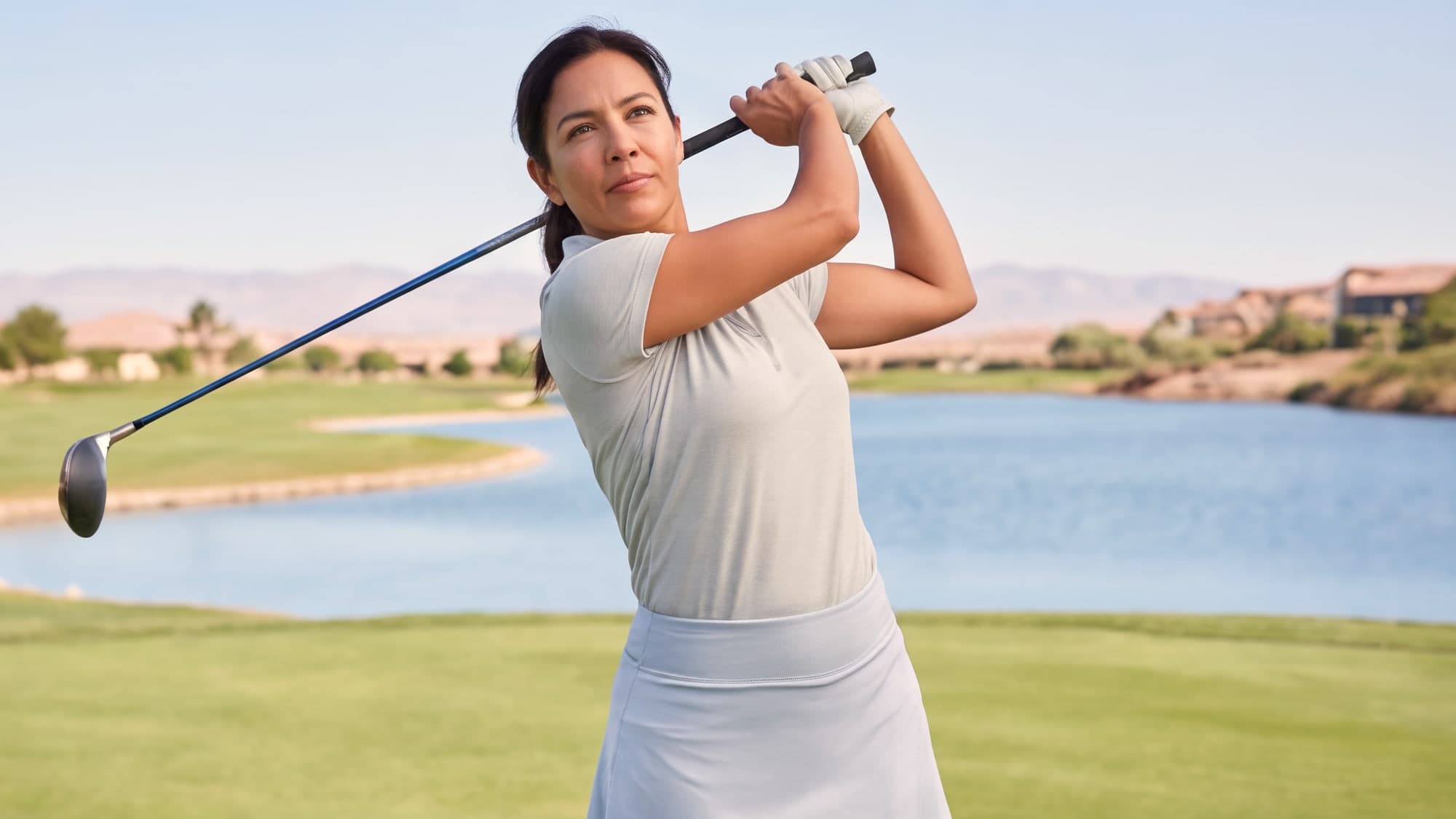 A woman finishing a golf swing on a fairway with palms and still water behind