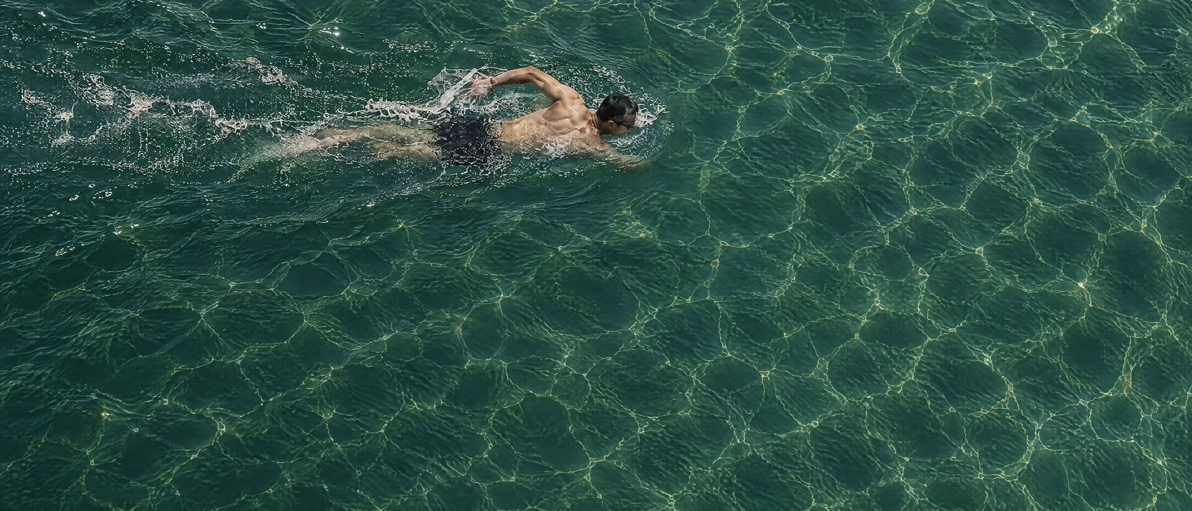 A swimmer crossing clear green water, seen from above