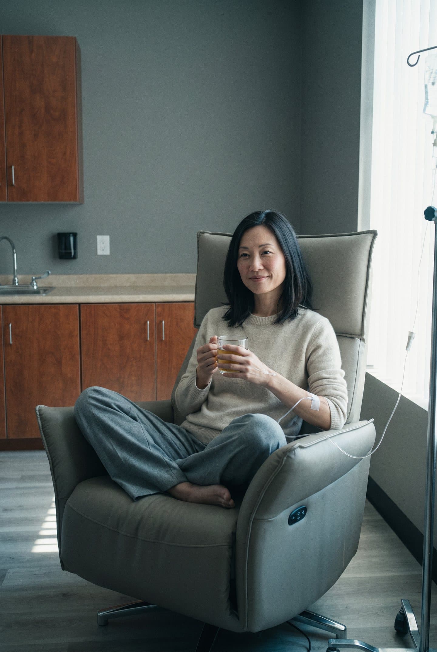 A woman holds a mug of tea in a recliner during an IV visit in the IV room at GIOSTAR Henderson