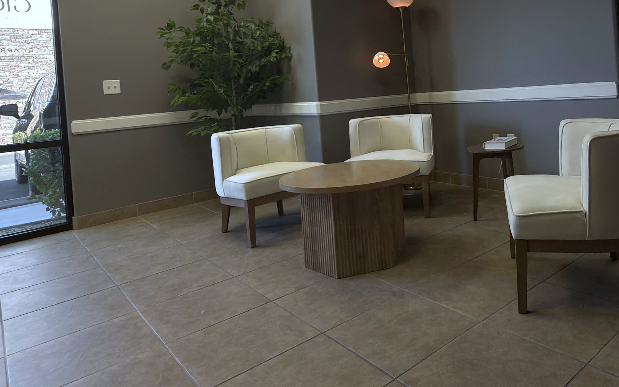 The waiting area at GIOSTAR Henderson, with cream armchairs around a round wood table and a floor lamp