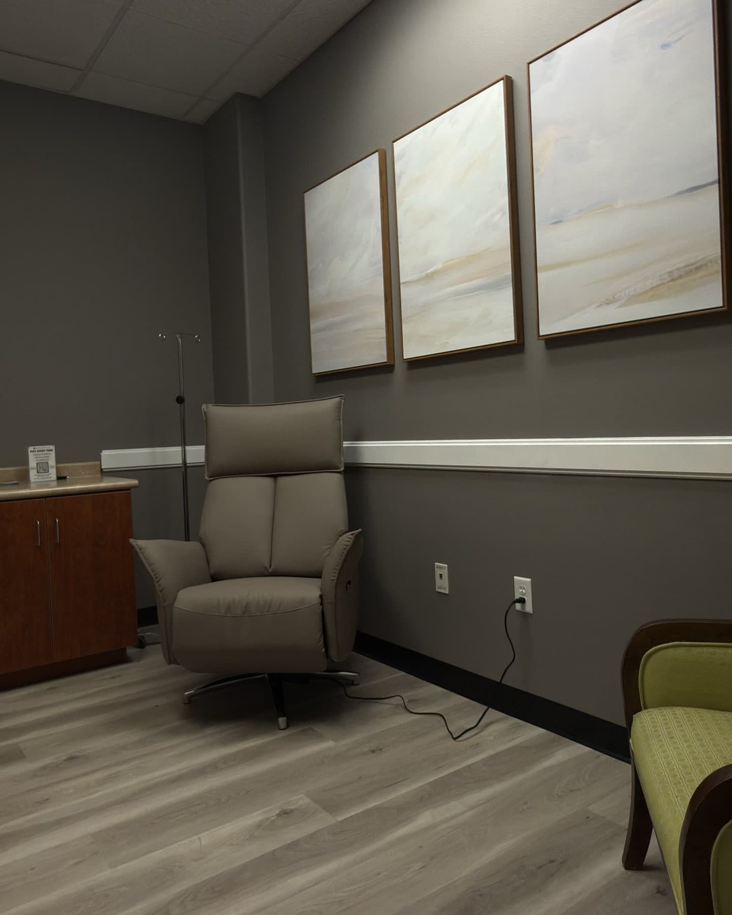 A private treatment room at GIOSTAR Henderson with a gray treatment recliner, an IV stand and three soft landscape paintings