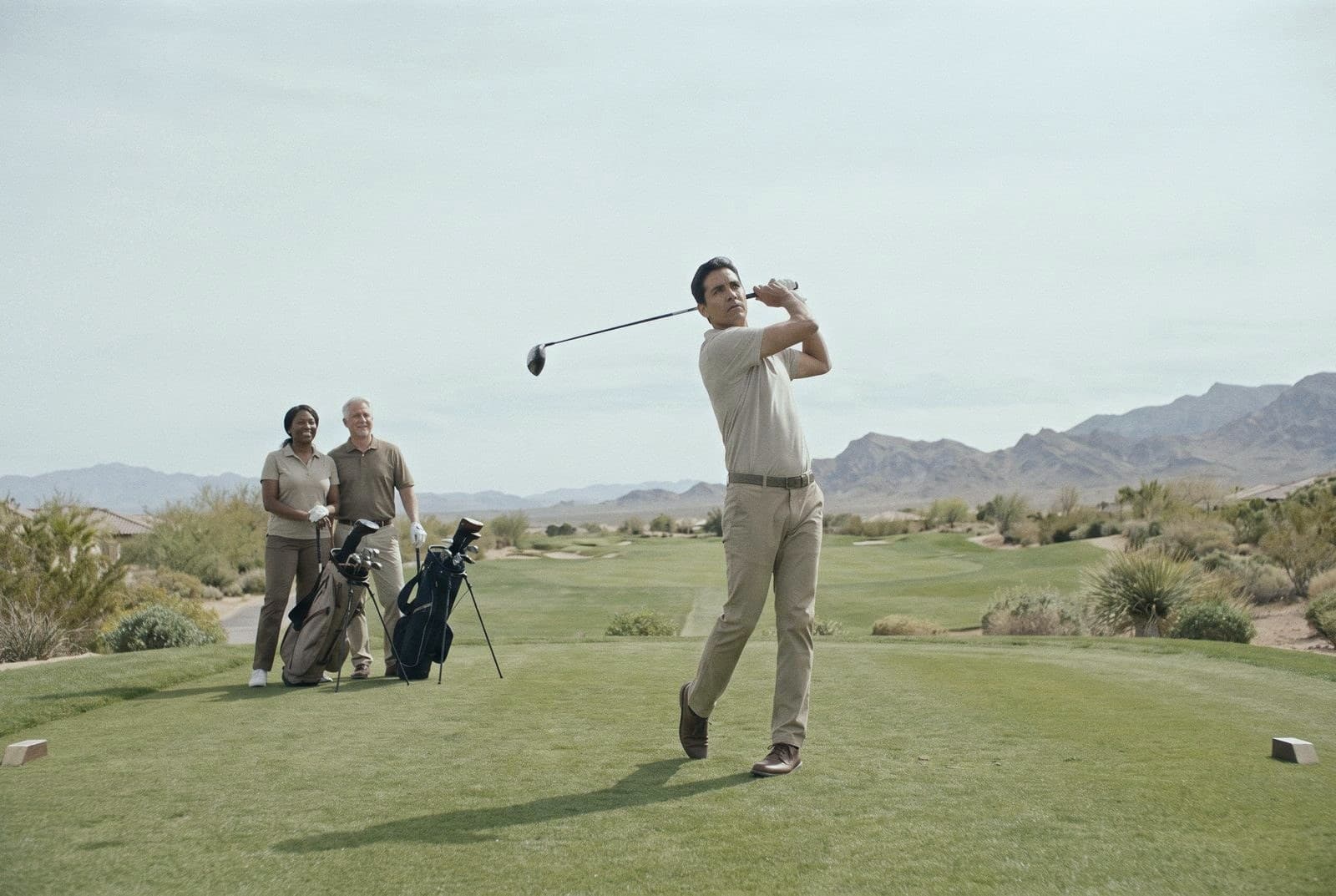 A man in his forties follows through on a tee shot on a desert golf course near Las Vegas while two friends watch