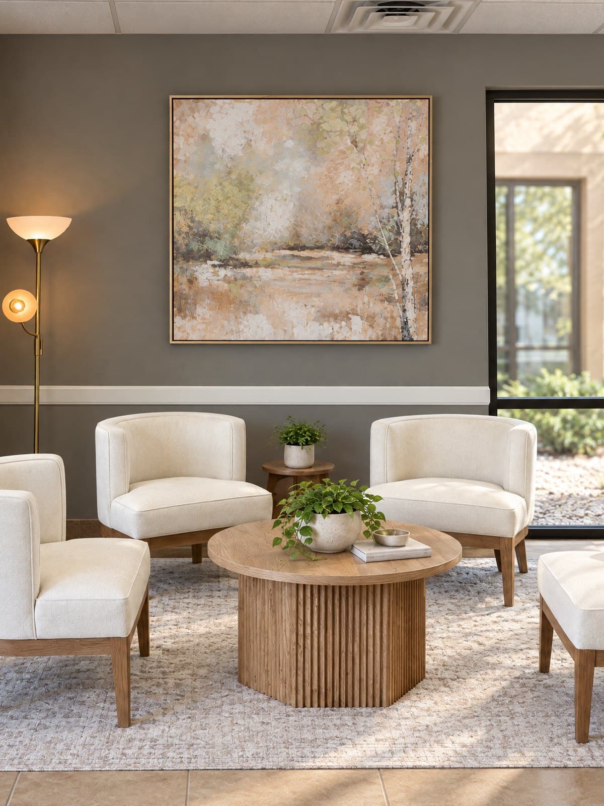 The lobby of GIOSTAR Longevity & Wellness in Henderson, with cream armchairs around a round wood table, a landscape painting and a window onto the courtyard